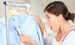 Shopping woman shocked over price tag. Funny shopper woman staring amazed at price. Mixed race Caucasian / Asian Chinese young female model in clothing shop.